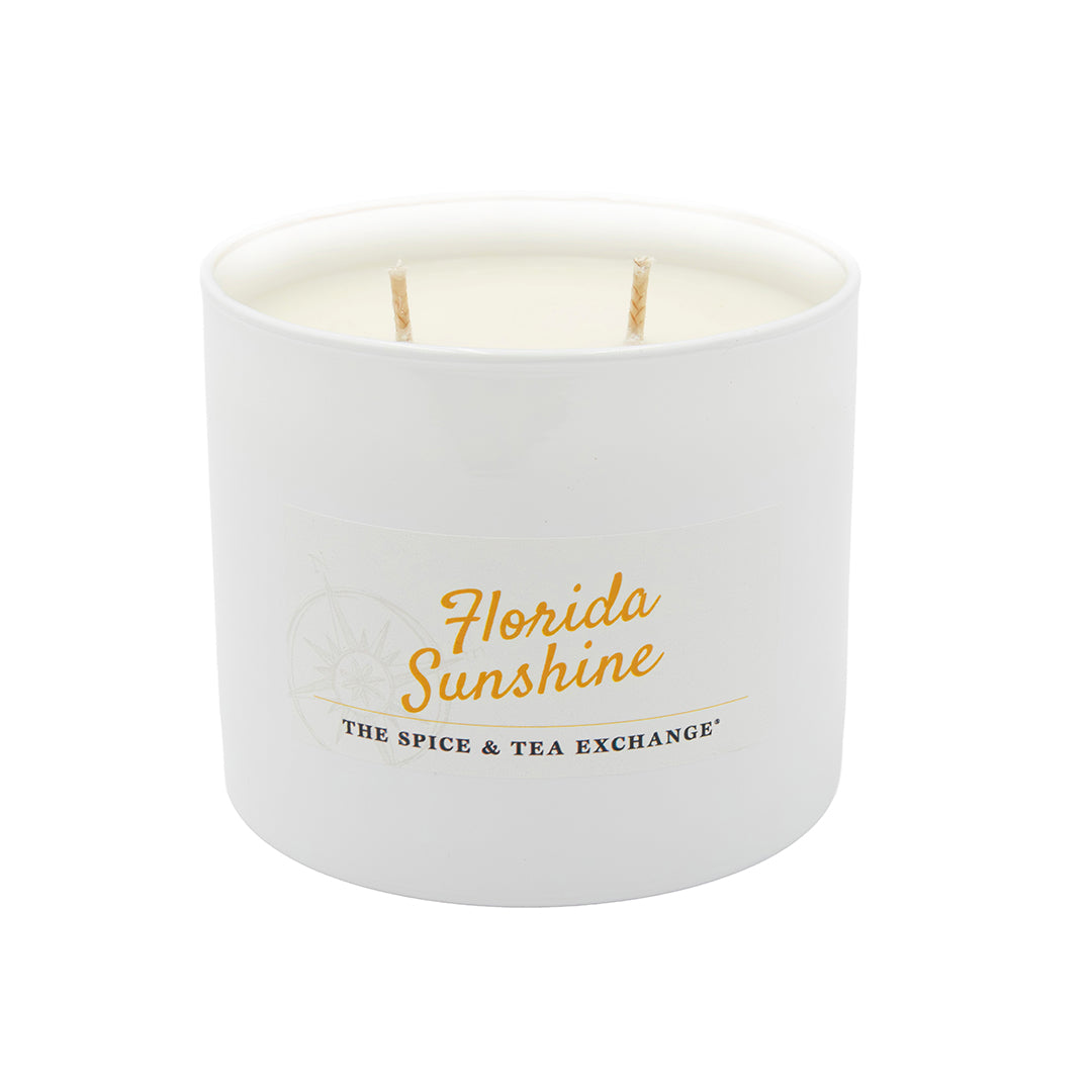 The Florida Sunshine Candle, a white soy candle with two wicks in a round container, features a citrusy scent inspired by the Florida Sunshine Spice Blend. The label reads "Florida Sunshine" from The Spice & Tea Exchange and is shown on a plain white background.